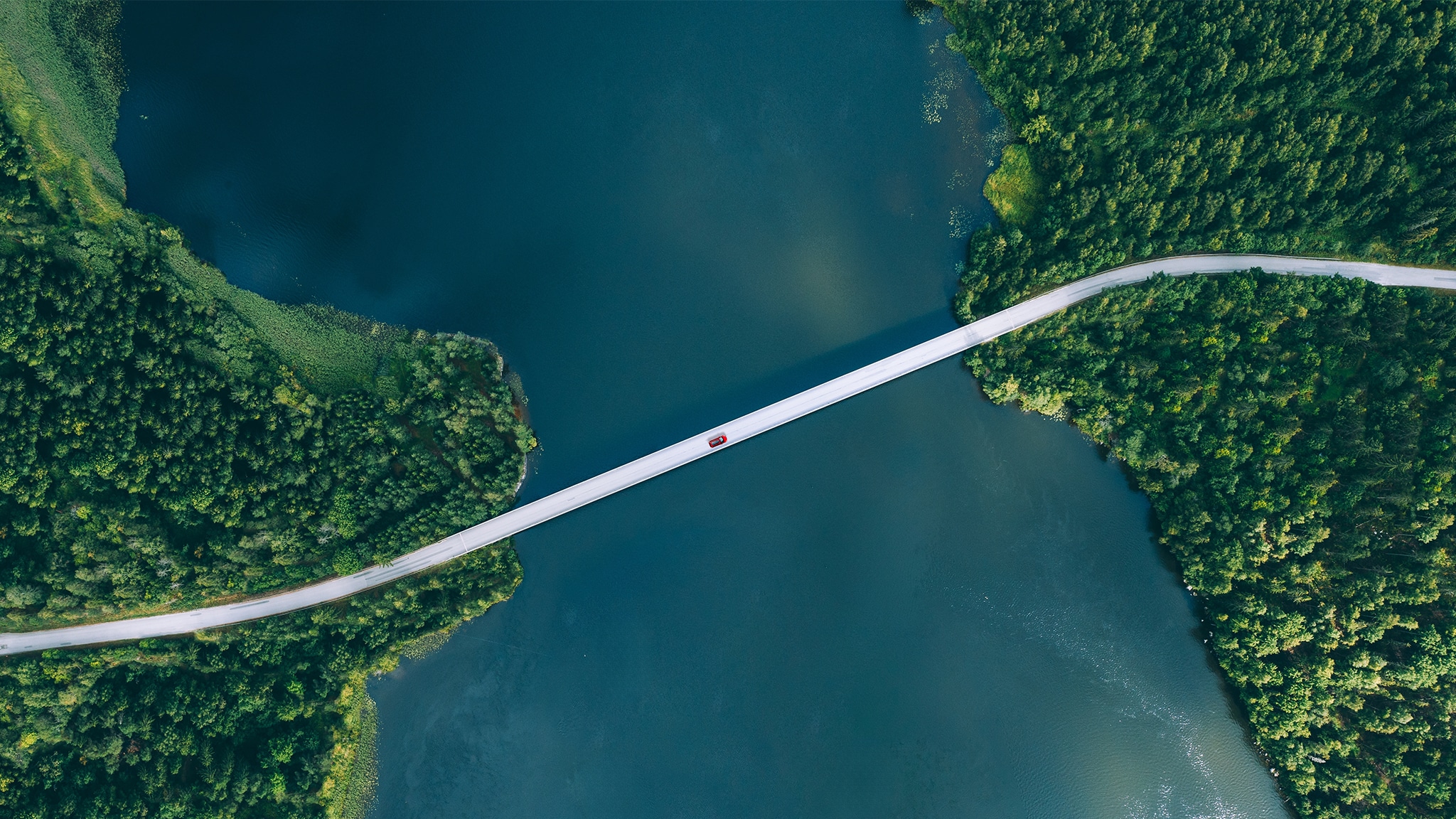 Eine Brücke, die über einen See führt, mit einem roten Auto darauf.