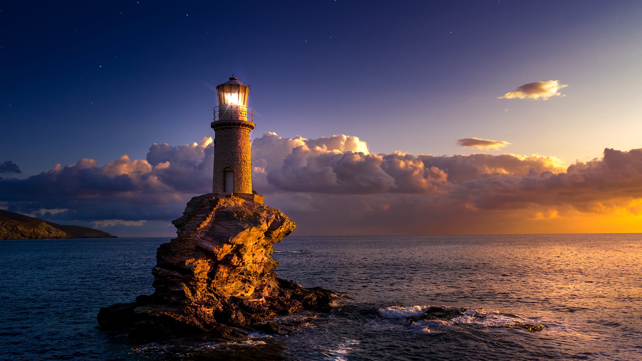 Leuchtturm auf einem Felsen mit Licht, umgeben von Wasser und Wolken am Abend.