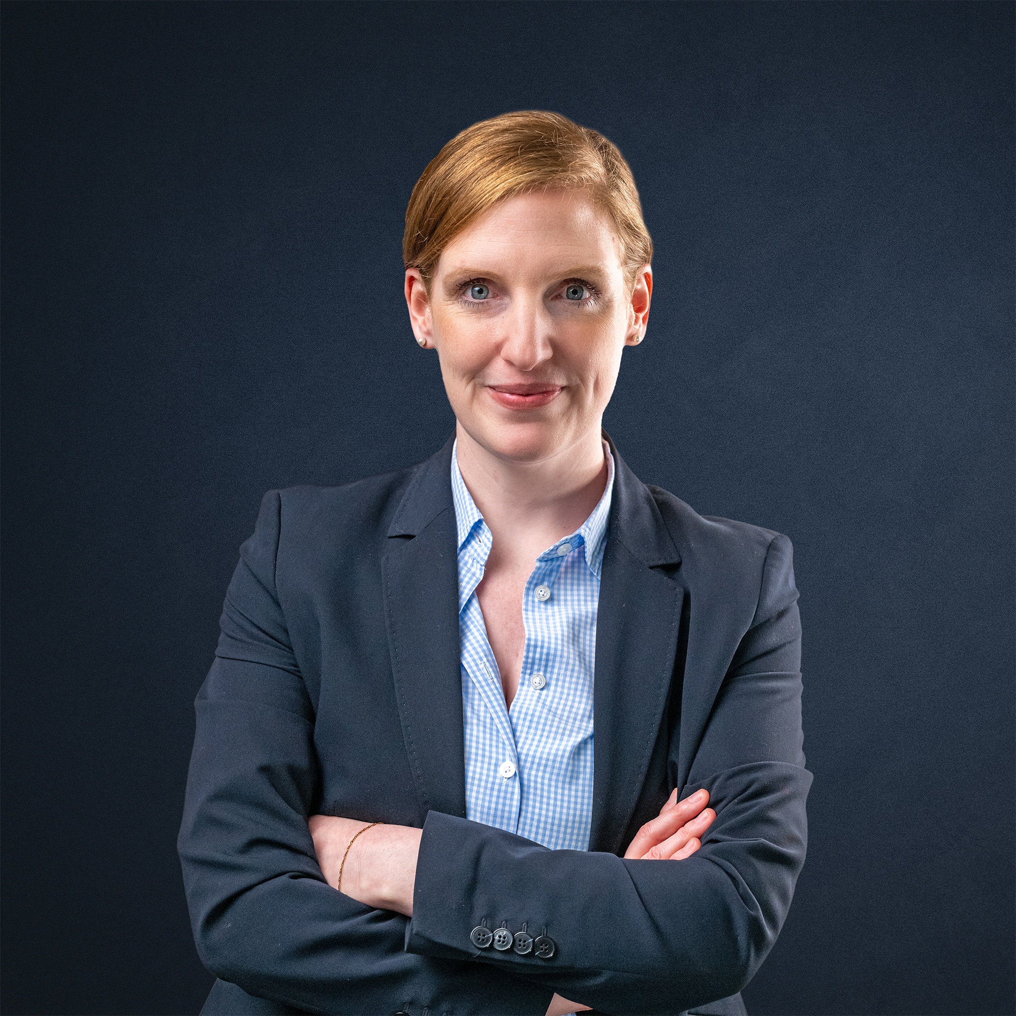 Frau mit blonden Haaren und einem blauen Anzug, die mit verschränkten Armen in die Kamera blickt.