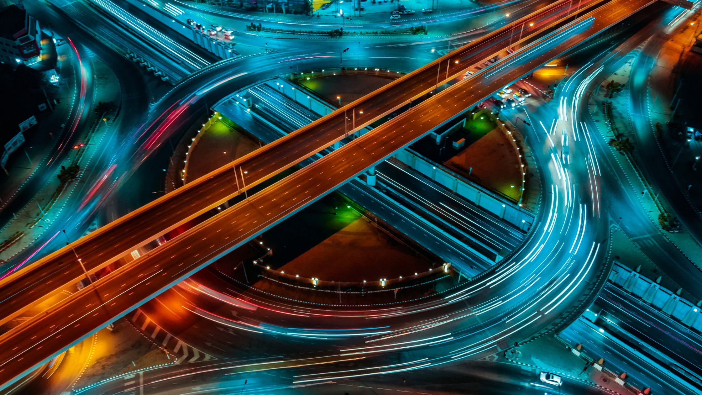 Luftaufnahme eines Verkehrskreisels mit beleuchteten Straßen und Fahrzeugbewegungen bei Nacht.