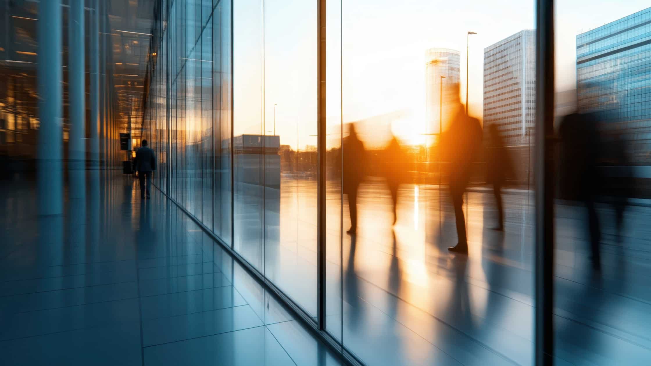 Silhouetten von Personen, die durch ein modernes Bürogebäude mit großen Fenstern gehen.