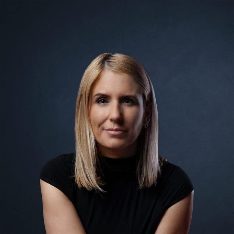 Porträt einer Frau mit blonden Haaren, die in einem schwarzen Oberteil posiert.